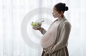 Happy pregnant young black woman eating vegetable salad at home