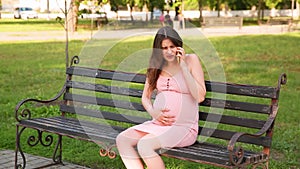 Happy Pregnant young woman chatting and text message to husband or family by using smartphone on city park bench