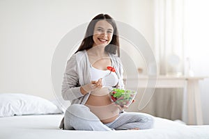 Happy pregnant young woman eating fresh salad at home