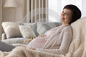 Happy pregnant young woman resting in armchair at home