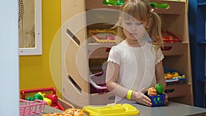 Happy preschool blond girl playing with toy kitchen at kids game center. Fun in kids room.