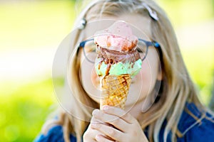 Happy preschool girl eating colorful ice cream in waffle cone on sunny summer day. Little toddler child eat icecream