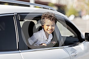 Happy preteen black boy looking out of open car window