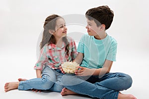 Happy preteen boy and girl eating popcorn, smiling talking to each other, isolated white background. Childhood. Family