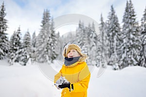 Happy preteen boy having fun playing with fresh snow during vacation in european Alps. Child dressed in warm clothes, hat, hand