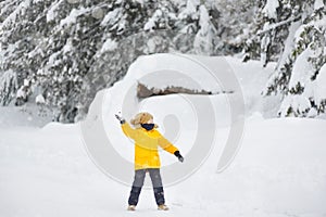 Happy preteen boy having fun playing with fresh snow during vacation in european Alps. Child dressed in warm clothes, hat, hand