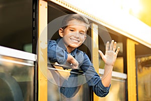 Happy preteen boy looking out of school bus window and waving hand
