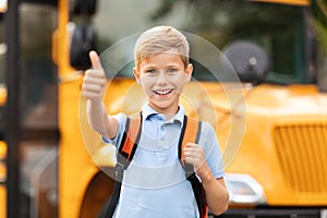 Happy Preteen Boy Showing Thumb Up While Standing Near School Bus Outdoors