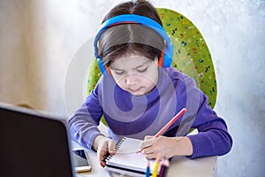 Happy preteen boy sitting on the couch or desk while using a laptop and headphones at home. Online chatting with his school