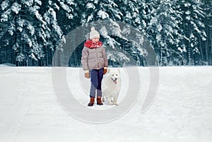 Happy preteen boy walking with his white Samoyed dog in winter snowy day over trees forest