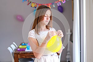 Happy preteen girl blowing yellow balloon decorating house preparing to kids birthday party