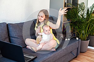 Happy preteen girl with her infant sister looking at laptop screen and gesturing hello while having video call.