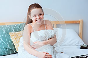 happy preteen girl sitting on bed and hugs cozy pillow.