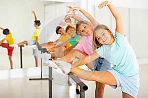 Happy preteen girl warming up near ballet bar during group class