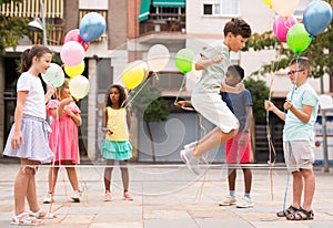 Happy preteen kids with balloons skipping on chinese jump rope in courtyard