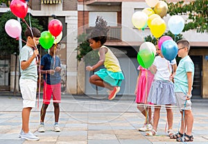 Happy preteen kids with balloons skipping on chinese jump rope in courtyard