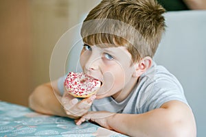 Happy preteen school boy eating sweet donut indoor. Blond child in domestic kitchen or in school canteen Cute kid and