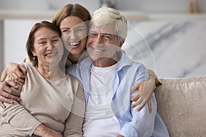 Happy pretty adult woman hugging positive older parents with love