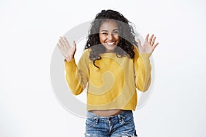 Happy pretty african american girl with curly hair showing excitement and happiness, greeting friends, waving raised