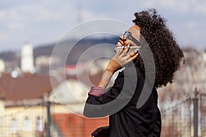 Happy pretty african businesswoman in eyeglasses is smiling and talking o nthe mobile phone at the blurred background of