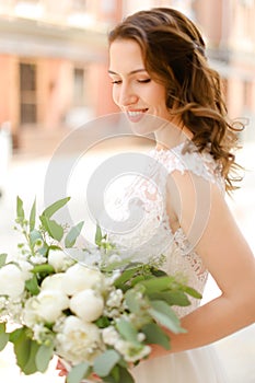 Happy pretty bride keeping bouquet of flowers and wearing white dress.