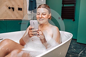 Happy pretty Caucasian woman using mobile phone while having a bath at home.