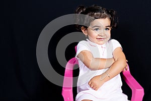 Happy pretty child girl sit on pink seat on black background with copy space