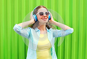 Happy pretty cool woman listens to music in headphones over green