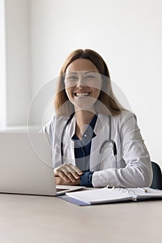 Happy pretty doctor woman sitting at work table in hospital