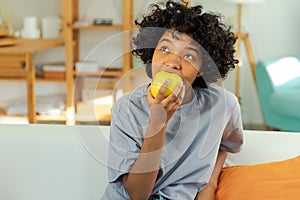 Happy pretty girl biting green apple at home. Beautiful african american young woman eating fresh fruit and smiling