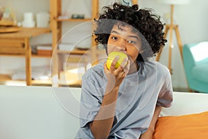 Happy pretty girl biting green apple at home. Beautiful african american young woman eating fresh fruit and smiling
