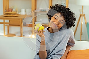 Happy pretty girl biting green apple at home. Beautiful african american young woman eating fresh fruit and smiling