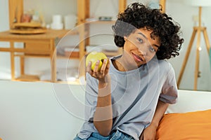 Happy pretty girl biting green apple at home. Beautiful african american young woman eating fresh fruit and smiling