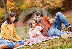 Happy pretty girl sitting in the grass with her parents and smil