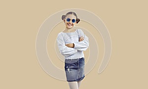 Happy pretty girl in trendy casual outfit and sunglasses posing on beige background