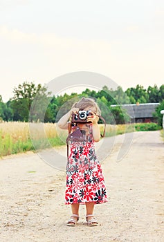 Happy Cute  little girl in retro outfit taking pictures with old film camera