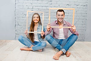 Happy pretty man and woman sitting barefoot on the floor with wooden frames