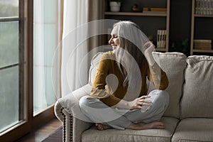 Happy pretty mature grey haired woman resting on cozy sofa