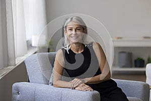 Happy pretty mature woman sitting in armchair, looking at camera