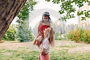 Happy pretty mother playing and riding on her shoulder her daughter in the park. Happy kid having fun with her mom enjoying the