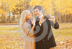 Happy pretty smiling young couple taking picture self portrait on smarphone outdoors in sunny autumn