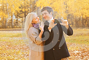Happy pretty smiling young couple taking picture self portrait on smarphone outdoors in sunny autumn photo
