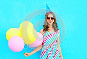 Happy pretty smiling young woman in a birthday cap with an air colorful balloons over blue background