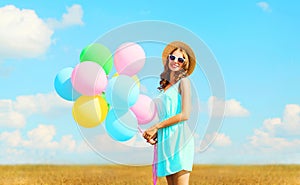 Happy pretty smiling young woman holds an air colorful balloons enjoying a summer day on a meadow blue sky