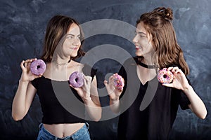 Happy pretty teenage girls with donuts having fun. Portrait of joyful girls with donuts on black background. Good mood, diet