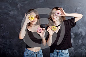 Happy pretty teenage girls with donuts having fun. Portrait of joyful girls with donuts on black background. Good mood, diet