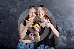 Happy pretty teenage girls with donuts having fun. Portrait of joyful girls with donuts on black background. Good mood, diet