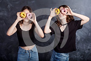 Happy pretty teenage girls with donuts having fun. Portrait of joyful girls with donuts on black background. Good mood, diet