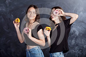 Happy pretty teenage girls with donuts having fun. Portrait of joyful girls with donuts on black background. Good mood, diet