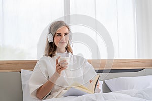 Happy pretty woman in earphones listening to music and singing while sitting on bed